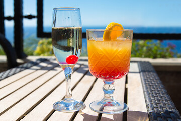 Two glasses with alcoholic drinks on a table by the sea.
