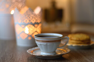 Plate with peanut butter cookies, cup of tea or coffee, open book, reading glasses and lit candles on the table. Selective focus.