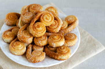 Puff pastry cookies with sugar on a white plate and linen napkin. The concept of homemade baking. Horizontal orientation. Selective focus