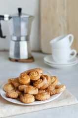 Puff pastry cookies with sugar on a white plate with a geyser coffee maker and two white cups. The concept of homemade baking. Vertical orientation. Selective focus