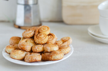Puff pastry cookies with sugar on a white plate with a geyser coffee maker and two white cups. The concept of homemade baking. copy space Horizontal orientation. Selective focus