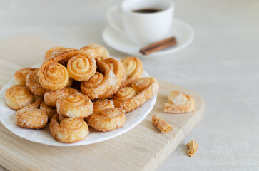 Puff pastry cookies with sugar on a white plate with a small white cup with coffee and a cinnamon stick. The concept of homemade baking. copy space Horizontal orientation. Selective focus