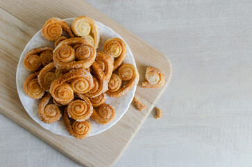 Puff pastry cookies with sugar on a white plate on a wooden cutting board. The concept of homemade baking. copy space Horizontal orientation. Top view. Selective focus