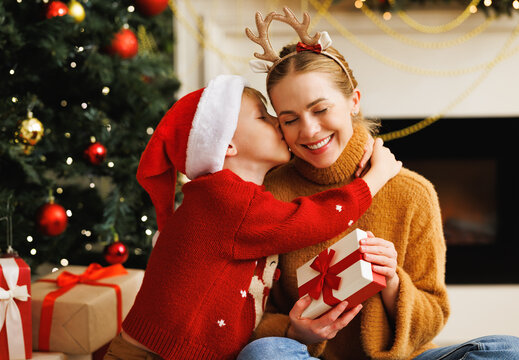 Cute child  smiling embracing and kissing mother opening christmas presents together