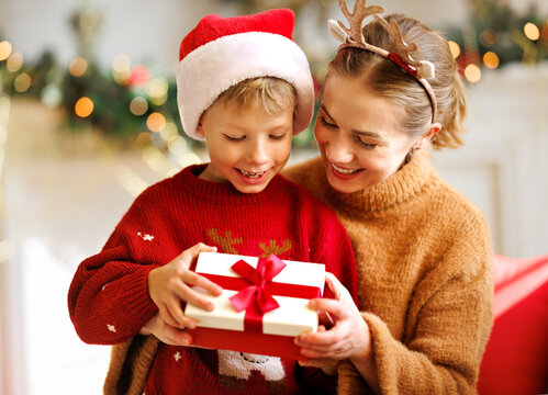 Cute child and smiling mother opening christmas presents together