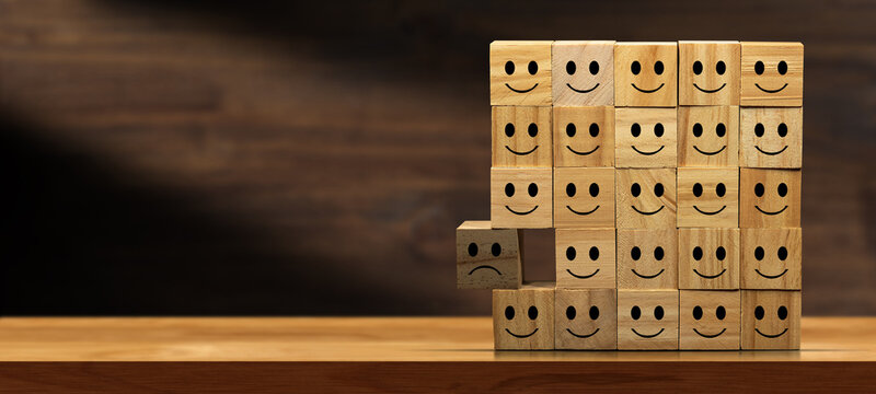 Large group of happy smiley faces and a sad one. Group of wooden blocks on a table with copy space. Concept of sadness, exclusion and depression.