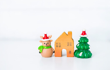 Cute little reindeer doll and wooden house with Christmas tree on white background, decoration item, festive season concept