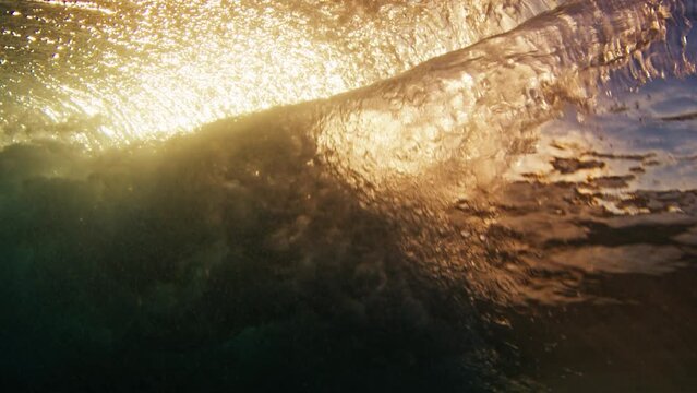 Underwater view of the ocean wave breaking on the shore at sunset.