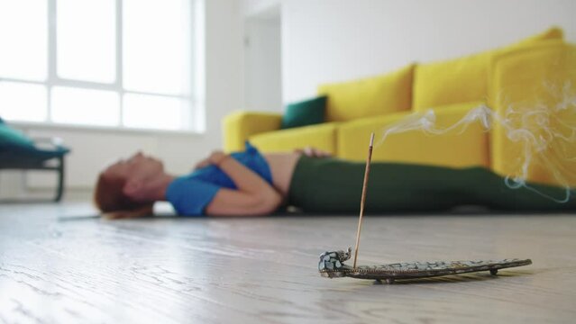 Adult woman lies on the floor and doing breathing practices - smoldering incense on the foreground
