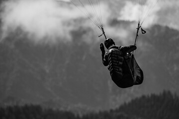 Grayscale shot of a tourist paragliding with mountains in the background