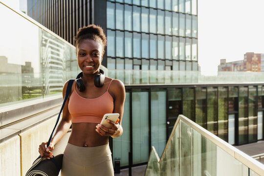 Young beautiful smiling fit afro woman with phone and mat