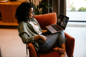 African woman smiling while making conference call on laptop in cozy apartment