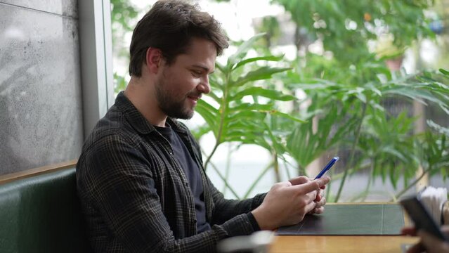 Young Man Holding Phone At Coffee Shop Staring At Screen