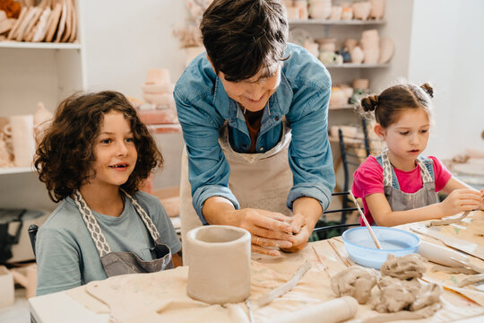 Mature female teacher sculpting with kids at ceramics workshop