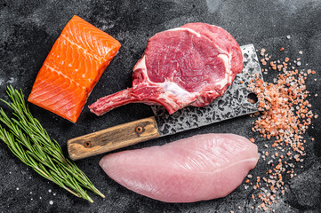 Butcher raw steaks - salmon, beef and turkey breast fillet on a meat cleaver. Black background. Top...