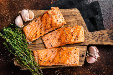 Griiled salmon fillets, fish steaks on wooden board with thyme. Dark background. Top view