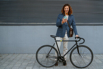 Fototapeta na wymiar Young ginger man using mobile phone while standing with bicycle outdoors