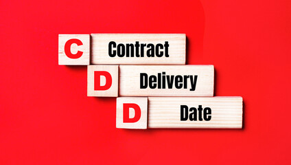 On a bright red background, wooden cubes and blocks with the text CDD Contract Delivery Date. Manufacturing of wooden toys.