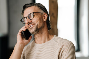 Closeup of middle-aged man smiling while talking on cellphone indoors