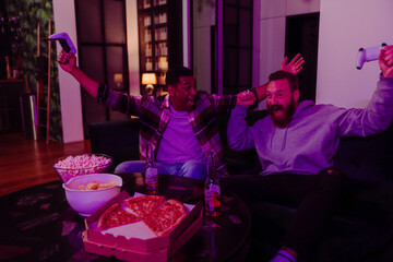 Two male friends gesturing as winners while playing video game in dark living room