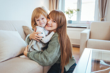 Happy loving family. mother and child girl playing, kissing and hugging. Attractive woman and little girl sitting on comfortable couch at home. 