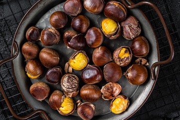 Cracked roast chestnuts served in a tray. Black background. Top view
