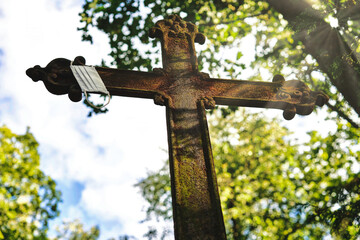 A rusty metal cross with a facemask hanging on it in an old cemetery. Beautiful sun rays illuminate it.