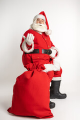 Santa Claus with a beard and mustache sits with a bag full of gifts. The bag of gifts is in the foreground. Christmas is coming. White background.