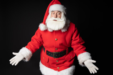 Santa Claus did not understand where everything had gone. Santa demonstrates a mistake and uncertainty will spread his arms to the sides. Portrait on a black background.