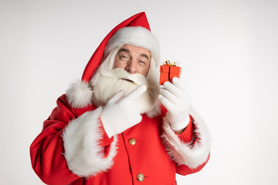Real Santa Claus points the finger of his right hand at a box with a gift on a white background.