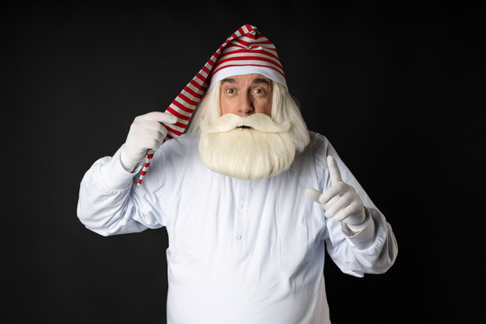 Santa Claus in his pajamas looks attentively directly into the camera holding his hat and gesturing with his hand. Sleepy and surprised Santa Claus. Concept for Christmas, just woke up Santa Claus.