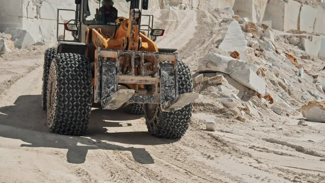 Unrecognizable man driving heavy-duty vehicle at work in marble quarry on sunny summer day, using loader machine for stones transportation