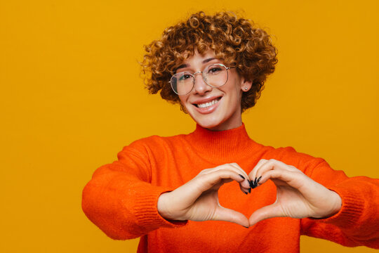 Joyful mature woman make heart love gesture isolated over yellow background