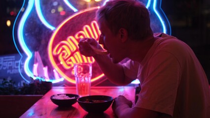A male tourist enjoys delicious spicy food at a Pan-Asian restaurant. Portrait of a man in neon...