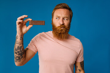 White bearded man eating chocolate bar isolated on blue background