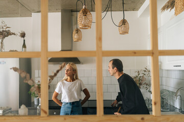 Remote view of angry husband scolding, raising voice, yelling at ignoring young girlfriend wife standing in kitchen room. Young Caucasian couple quarrelling yelling at home. Concept of family problems