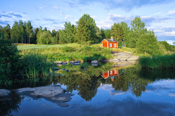 A small red cottage reflected in the river on a beautiful summer evening. An old traditional...