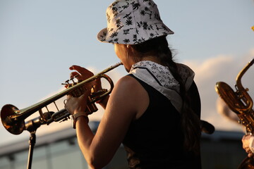 A person playing the trumpet in a hat outdoors back view