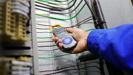 Obraz premium Hand closeup of electrical engineer to use digital ampere meter to measurement electrical current from power cable in feeder cabinet in electricity substation, industrial and energy concept
