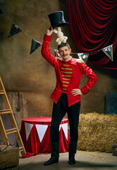 Illusionist. Vintage portrait of male retro circus entertainer expresses rejoice and announces start of show over dark retro circus backstage background.