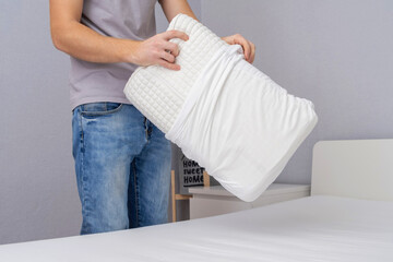 A man tucks an orthopedic pillow with a fresh bright white pillowcase. Making bed with fresh bed...
