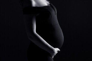 pregnancy woman in black dress on a black background, studio pregnancy shoot