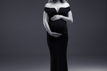 A pregnant woman stands on a grey background. A pregnant woman. Studio pregnancy photo shoot....