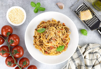 Spaghetti bolognese with fresh basil, tomatoes, garlic and parmesan cheese on a gray background. Pasta with meat ragout. Italian food.