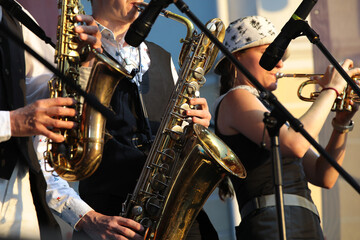 A group of jazz street musicians play saxophone and trumpet performing in the summer on a sunny day outdoors