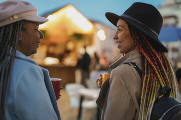 Happy african mother and daughter having fun together drinking hot tea outside at christmas markt