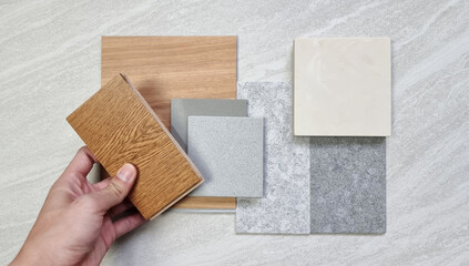 interior decorator holding oak engineering flooring sample. interior material mood board. combination of material samples including vinyl flooring tile, grey artificial stones, onyx marble tile.