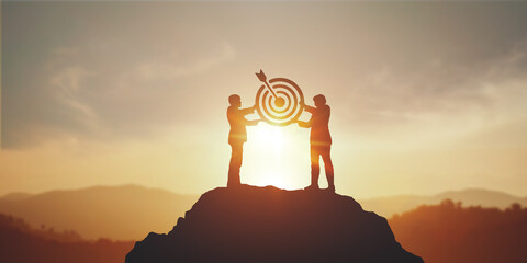 Fototapeta na wymiar Silhouette of two businessman holding a target board on top mountain. concept of aim, objective achievement, leadership and teamwork
