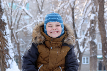 Portrait of an attractive boy outdoors in winter. He is dressed in a warm hat and jacket, closed his eyes, and smiles.