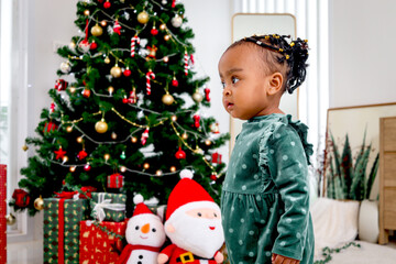 Portrait of adorable African American little girl child standing in living room with many gift boxes presents under Christmas tree, kid celebrating happy Christmas winter holiday